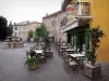 Embrun - Place Barthelon : terrasse de café, fontaine et maisons aux façades colorées de la vieille ville