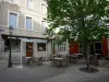 Embrun - Place de la Mazelière : terrasse de café, arbre, lampadaire et façades de maisons de la vieille ville