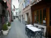 Embrun - Ruelle de la vieille ville avec terrasse de café, maisons et arbustes en pots