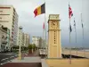 Les Sables-d'Olonne - Remblai, horloge (tour), drapeaux, promenade agrémentée de palmiers, rue, immeubles et plage de sable de la station balnéaire