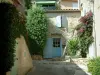 Ле-Кастелле - Цветущая бугенвиллия (бугенвиллия), кустарники, аллея с мольбертом и дома средневековой деревни