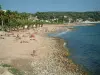 Bandol - Palmiers, plage de sable de la station balnéaire avec des estivants, galets, mer méditerranée, maisons et forêt en arrière-plan