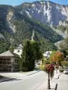Le Bourg-d'Oisans - Bell tower of the Saint-Laurent church, houses, lampposts and flowers in the village, mountain overhanging the place