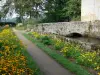 Castillo de Les Martinanches - Sendero bordeado de flores y el puente pequeño a través de un foso, en la comuna de Saint-Dier-d'Auvergne, en el Parque Natural Regional Livradois