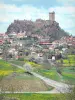Castillo de Polignac - Camino bordeado de prados en flor, con vistas a la fortaleza de Polignac encaramada en su colina de basalto y las casas del pueblo medieval debajo del castillo