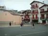 Ciboure - Frontón con jugadores de pelota vasca y casas blancas con contraventanas rojas de la ciudad vieja
