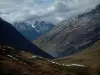 Col de la Croix-de-Fer pass - From the Croix-de-Fer road, view of alpine pastures (high meadows), a lake and mountains with snowy summits, cloudy sky (Grande Alpes (Alps) road)