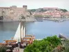 Collioure - Côte Vermeille : terrasse de café en premier plan avec vue sur la mer, le château royal, le fort Miradou, le port, la plage et la vieille ville de Collioure