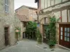 Cordes-sur-Ciel - Calle en cuesta empedrada de la ciudad medieval, rosales trepadores (rosas) y algunas casas con paredes de madera