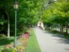 Coulommiers - Parque de los Capuchinos: sendero bordeado de bancas, árboles y flores, lámpara de la calle en primer plano