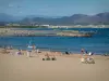 Fréjus - Fréjus-Plage : plage de sable avec des estivants, mer méditerranée, rochers, golfe de Fréjus et collines en arrière-plan