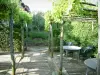 Gardens of the Notre-Dame d'Orsan priory - Tables and chairs on the pergola terrace, plants and trees in background