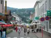 Gérardmer - Calle con casas, tiendas y terrazas de restaurantes, cabañas y forestales en el fondo