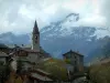 Lanslevillard - Torre de la iglesia y las casas de la aldea, montaña nevada en el fondo del cielo y nublado, en la Haute-Maurienne (zona periférica del Parque Nacional de la Vanoise)