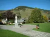 Megève - Winter and summer sports resort: garden with hopscotch game, statue, benches, lawns and trees, chalets, alpine pastures (high meadows) and forest in background