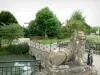 Mouzon - Jardins da abadia: leão de pedra esculpida, ponte sobre a água, canteiros e vegetação