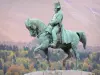 Napoléon Road - Bronze equestrian statue of Napoleon I in the meadow of the Rencontre meeting, trees with autumn colors in the background; in the town of Laffrey