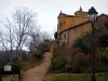 Oingt - Camino bordeado por árboles y arbustos, poste de luz, casa de piedra y la iglesia de la villa medieval, en la Tierra de Oro de Piedra (Beaujolais)