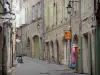 Pézenas - Old town: narrow paved street lined with shops and stone houses with green shutters