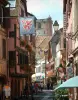 Ribeauvillé - Street with a suspended flag, colourful houses with windows decorated with flowers and the Bouchers tower (ancient belfry) in background