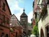 Riquewihr - Colourful half-timbered houses decorated with flowers and creepers, superior gateway (Obertor) in background