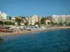 Saint-Raphaël - The Mediterranean Sea, sandy beach with tourists, parasols and sunbeds, palm trees, houses and buildings of the seaside resort