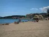 Sainte-Maxime - Plage de sable avec des estivants, mer méditerranée, pont, immeubles et maisons de la station balnéaire, nuages dans le ciel bleu