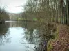 Suisse normande - Vallée de l'Orne : arbres se reflétant dans les eaux de la rivière, rive couverte de feuilles mortes et viaduc en arrière-plan