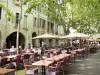 Uzès - Place aux Herbes: terrazas de los restaurantes, casas con soportales y plátanos (árboles)